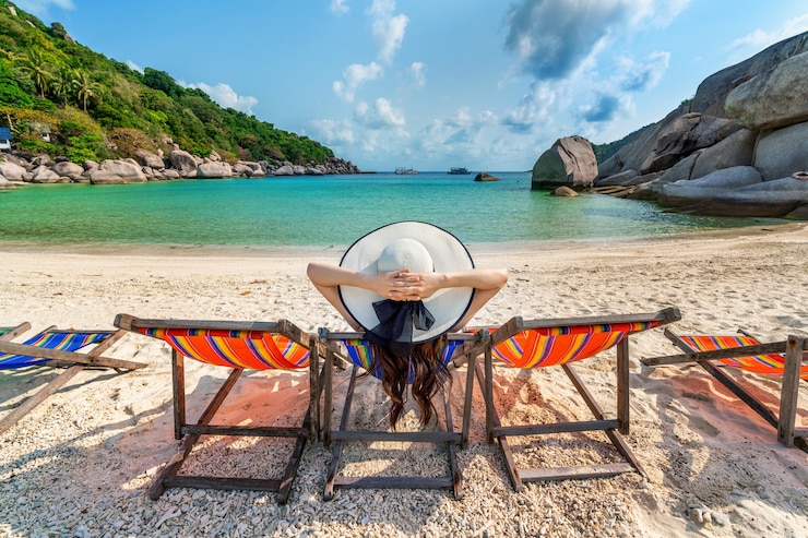 Femme avec chapeau assise sur des chaises de plage dans une belle plage tropicale.